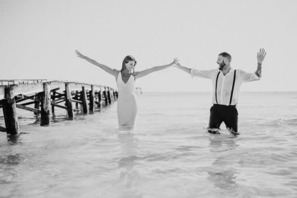 Happy bridal couple in the water rising up the arms